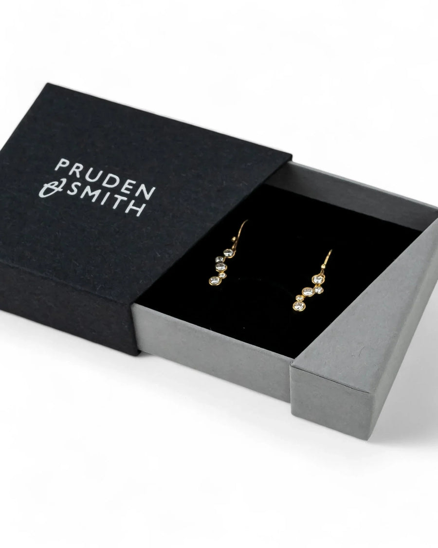 Gold drop earrings with multiple round diamonds in an open black gift box.