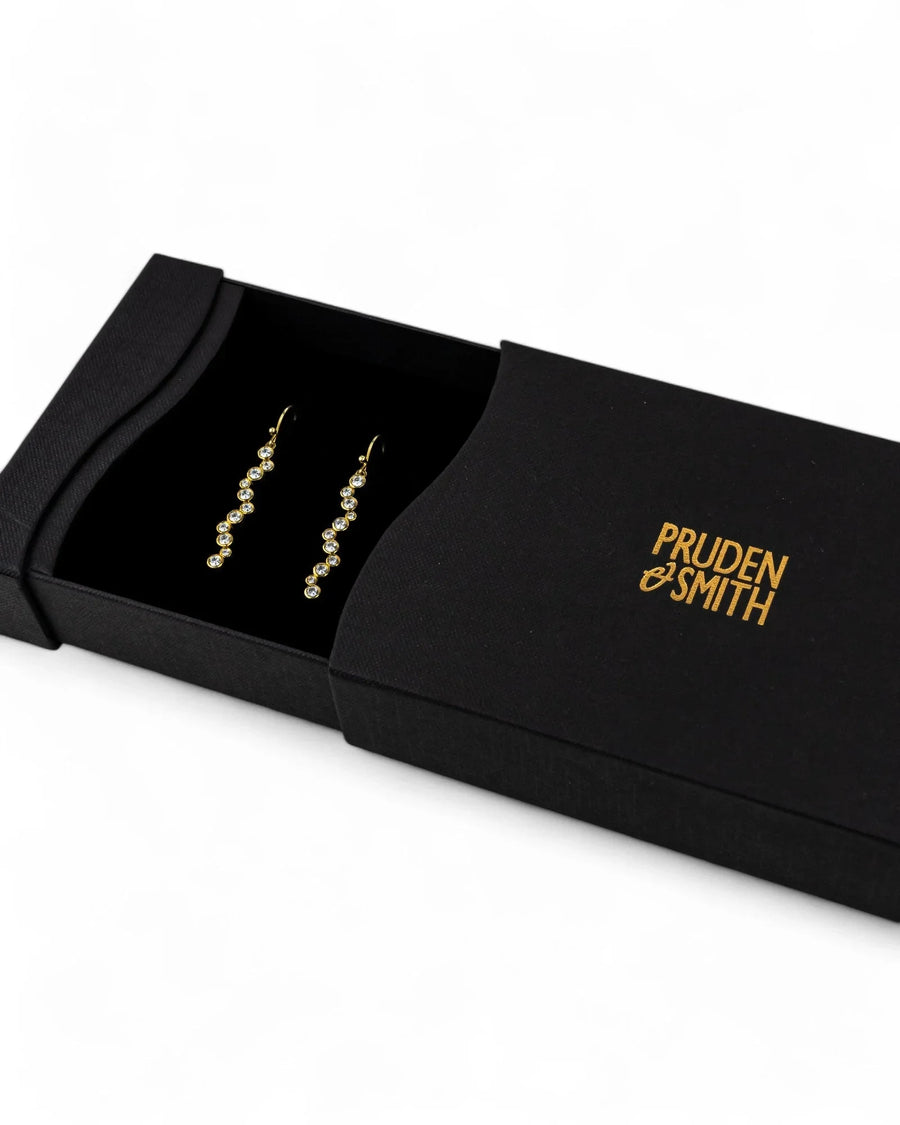 Gold drop earrings with clear gemstones in a black box.