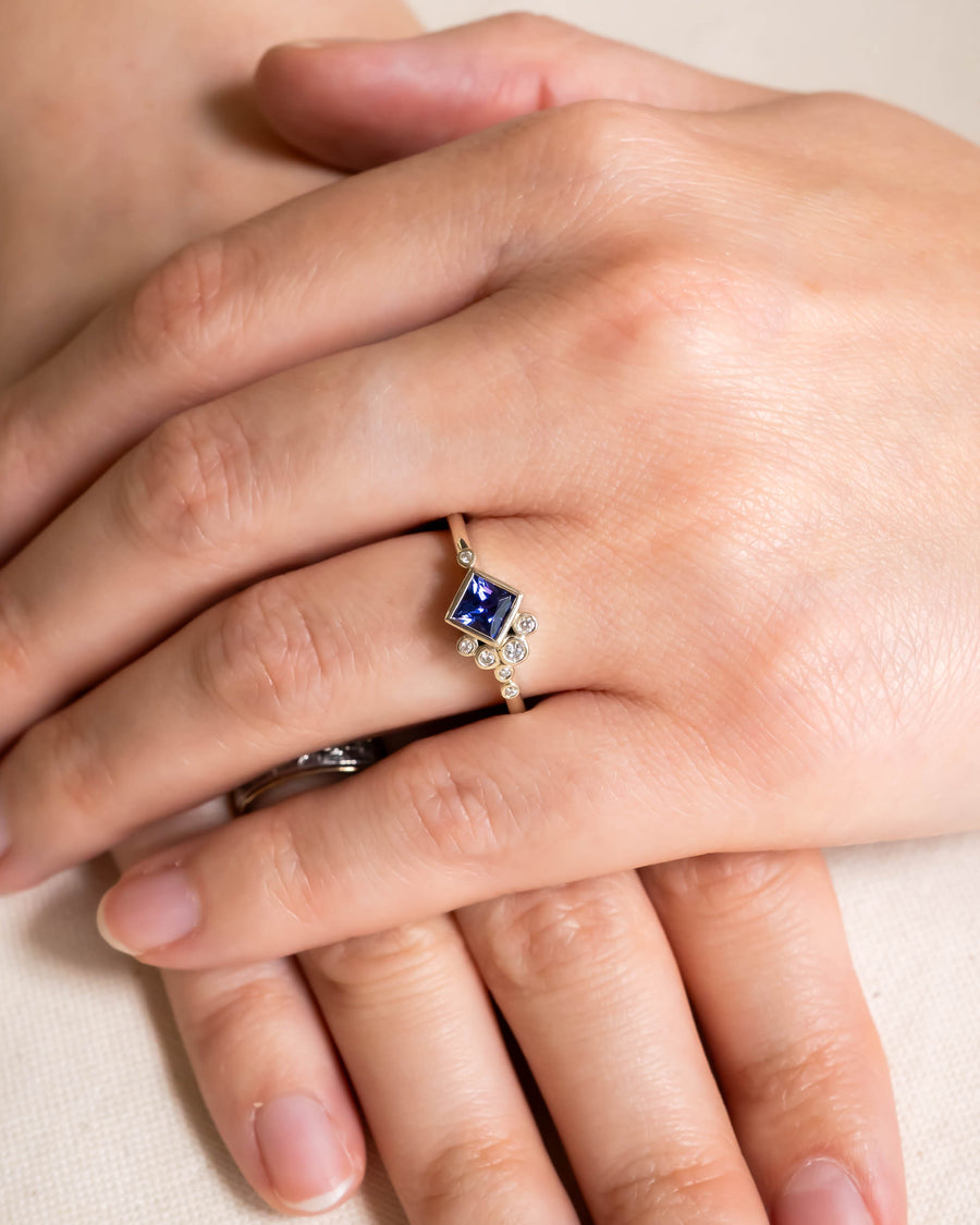 Gold engagement ring with a square blue gemstone and small diamonds.