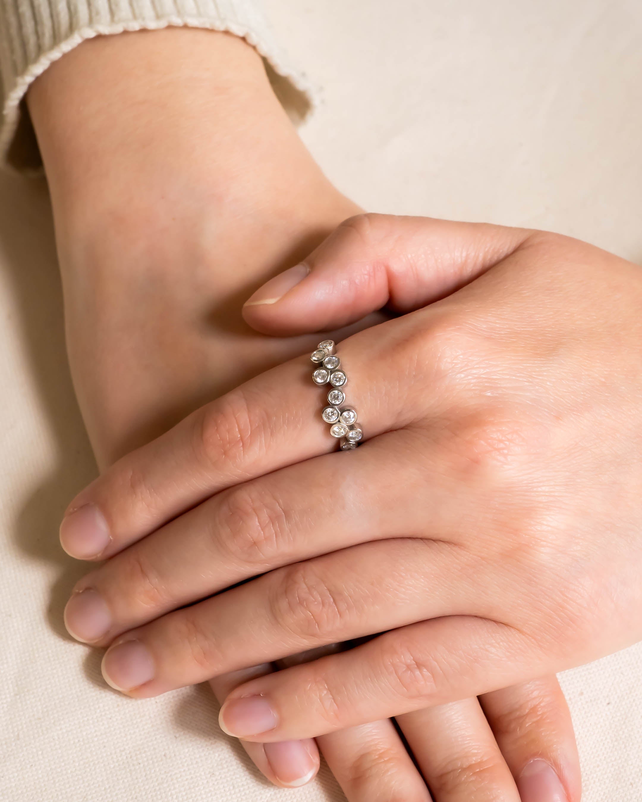 White gold half eternity ring with round diamonds in a bubble design on a hand.