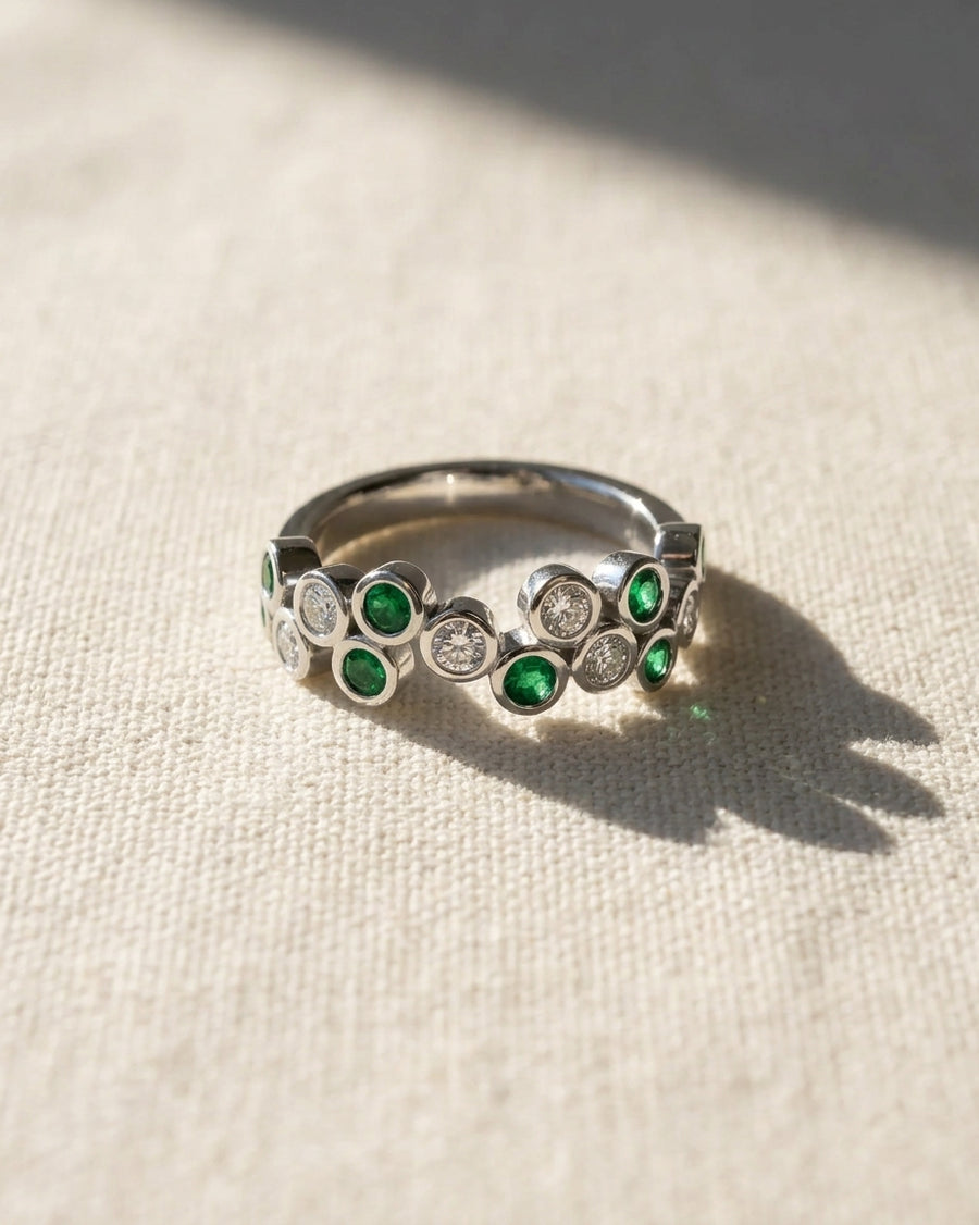 White gold half eternity ring with round emeralds and diamonds.
