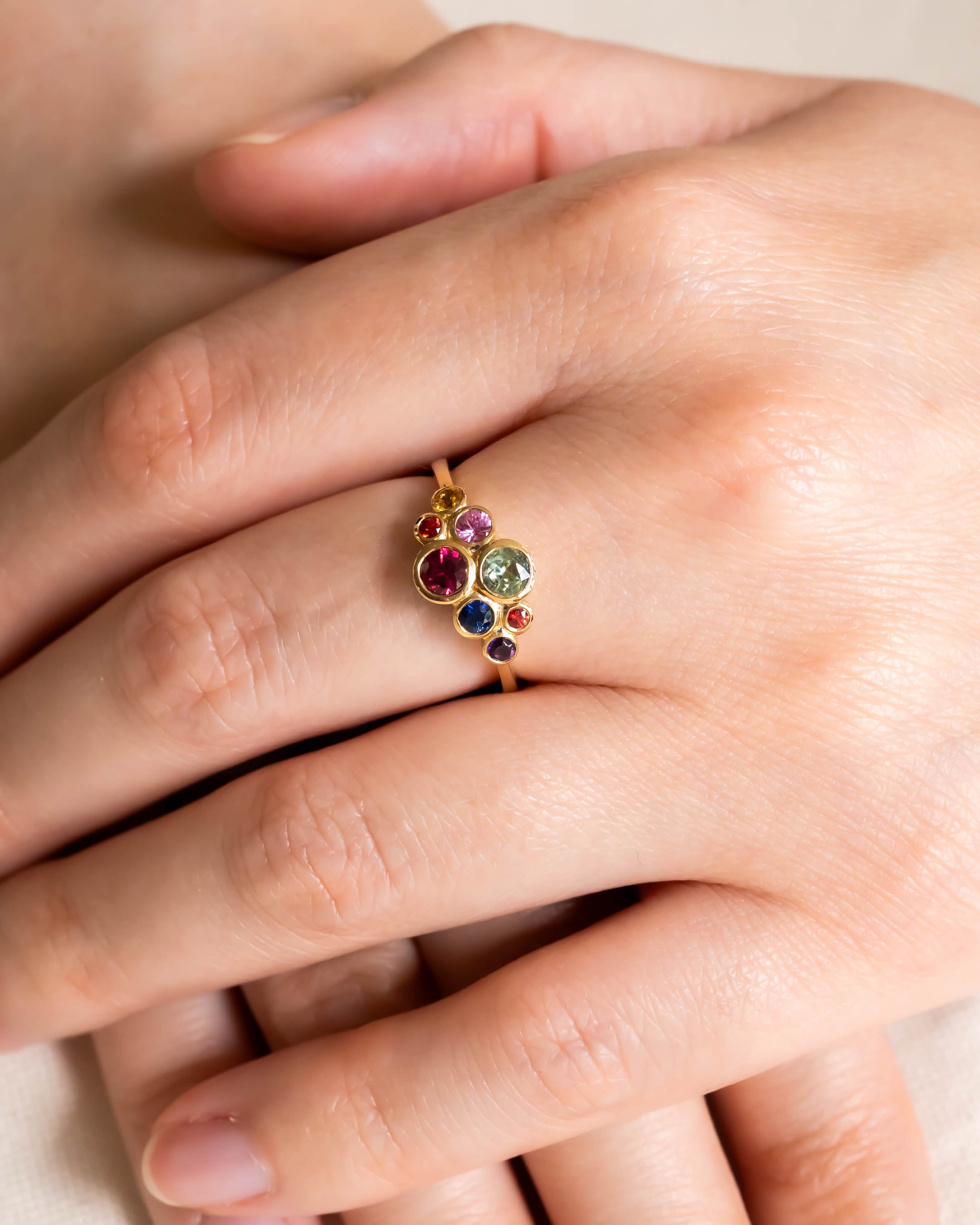 Gold ring with multi-coloured sapphire cluster design on a hand.