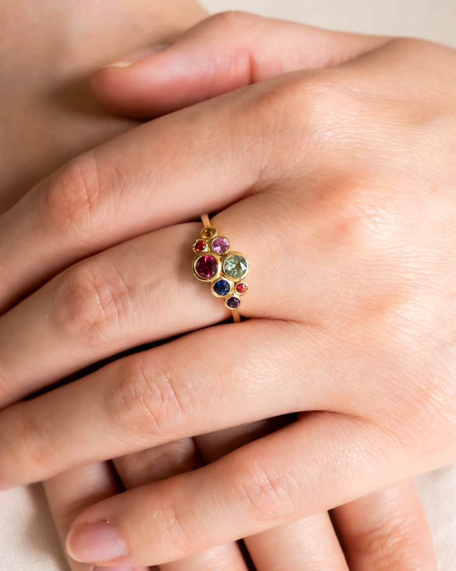 Gold ring with multi-coloured sapphire cluster design on a hand.