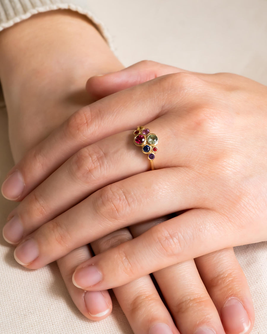 Gold ring with multi-coloured sapphire cluster design on a hand.