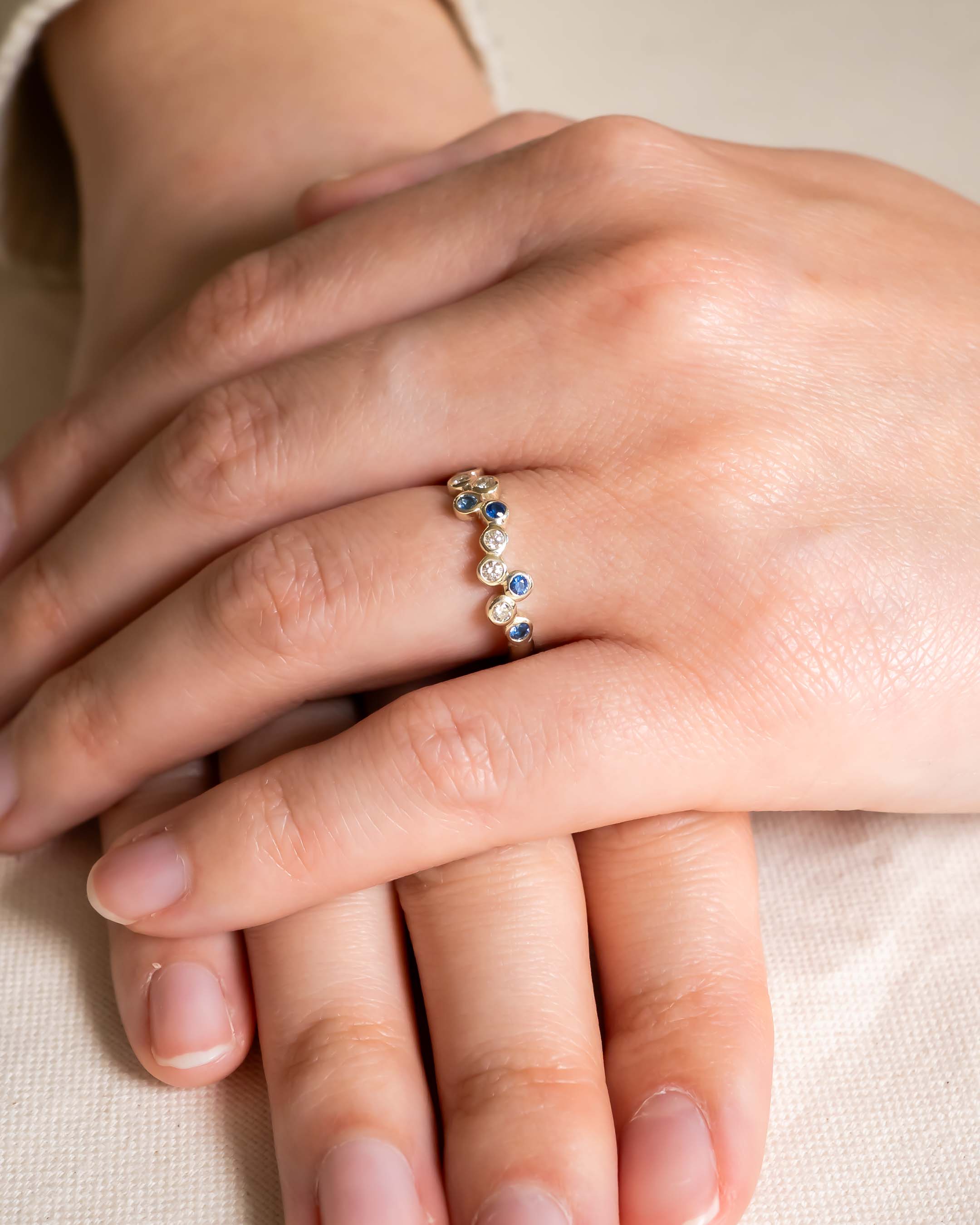 Gold half eternity ring with offset blue and clear gemstones.