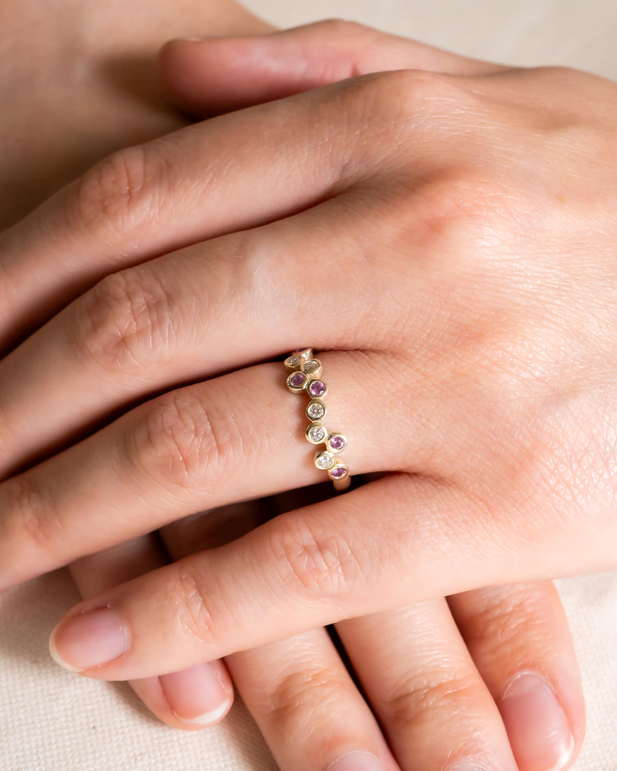 Gold offset half eternity ring with pink gemstones and diamonds.