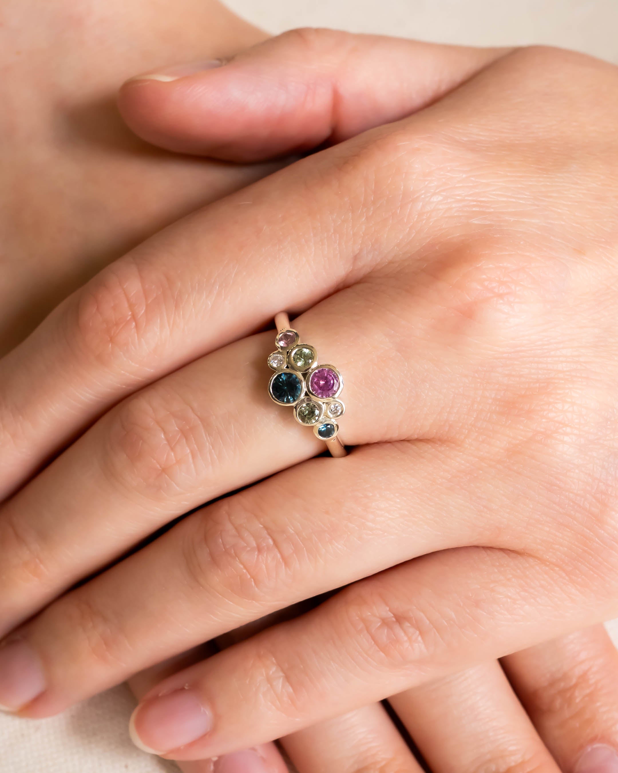 Gold ring with pink and teal sapphire cluster design on a hand.