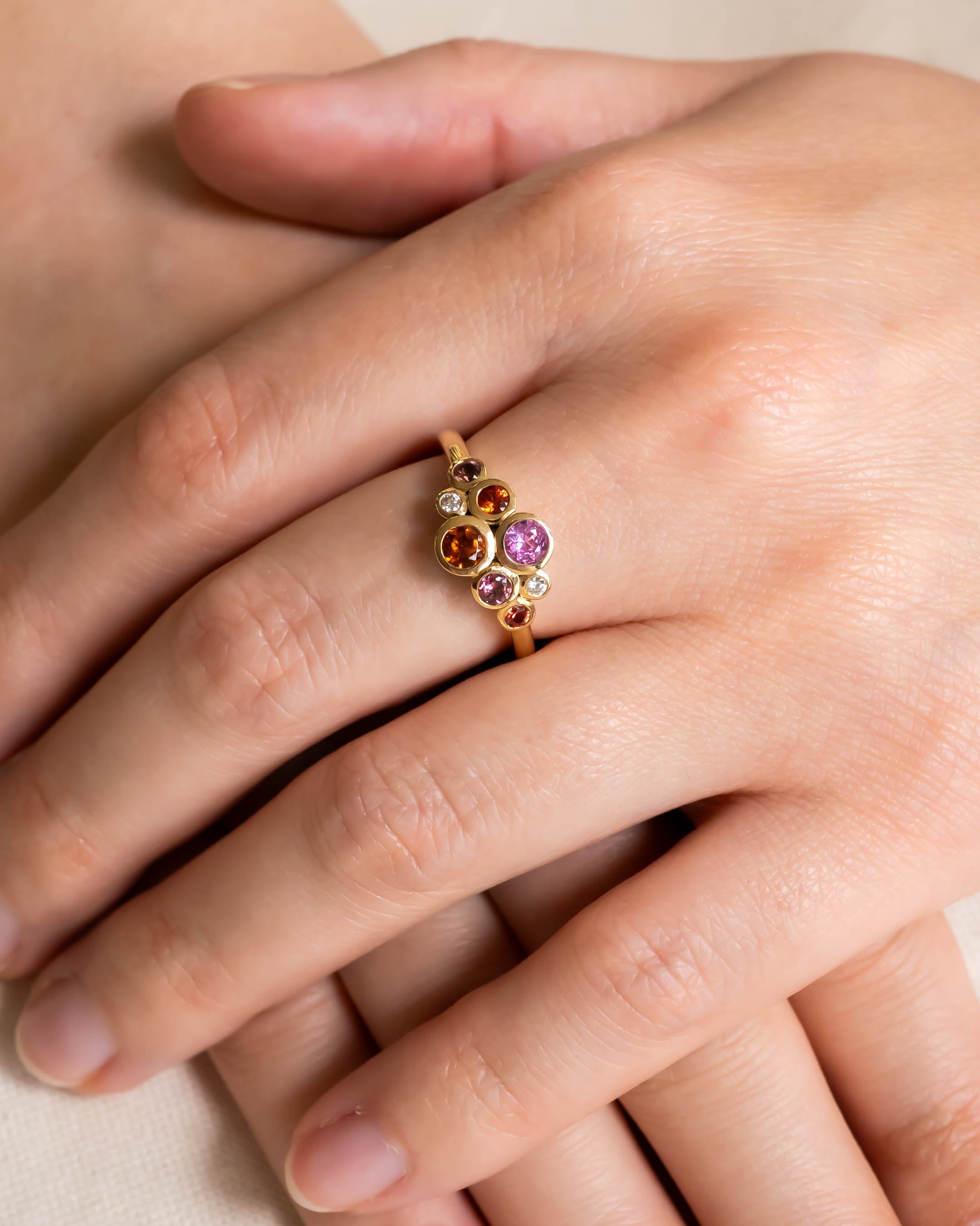 Gold cluster ring with pink tourmaline, citrine, and diamond gemstones on a hand.
