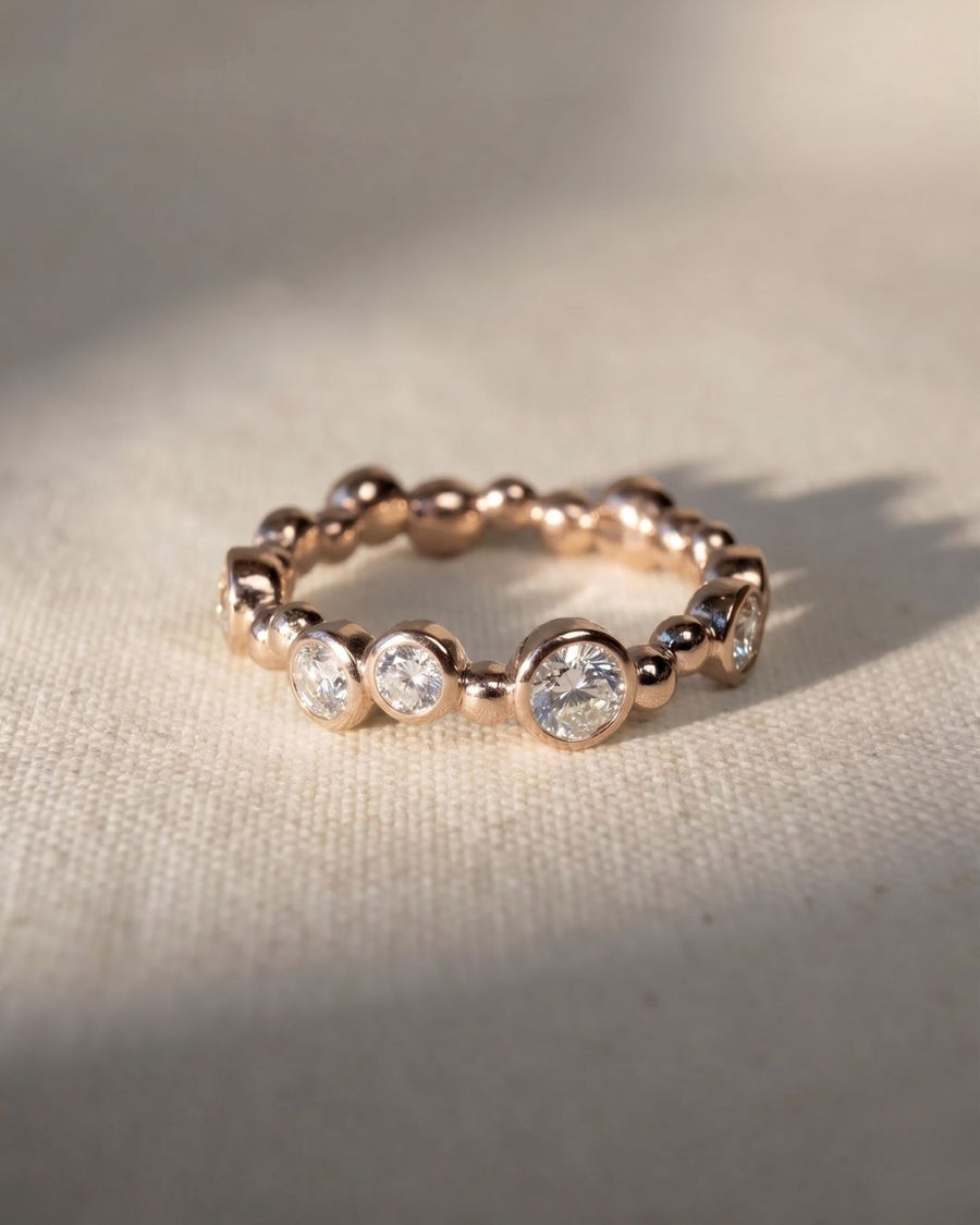 18ct rose gold eternity ring with random bezel-set round diamonds.