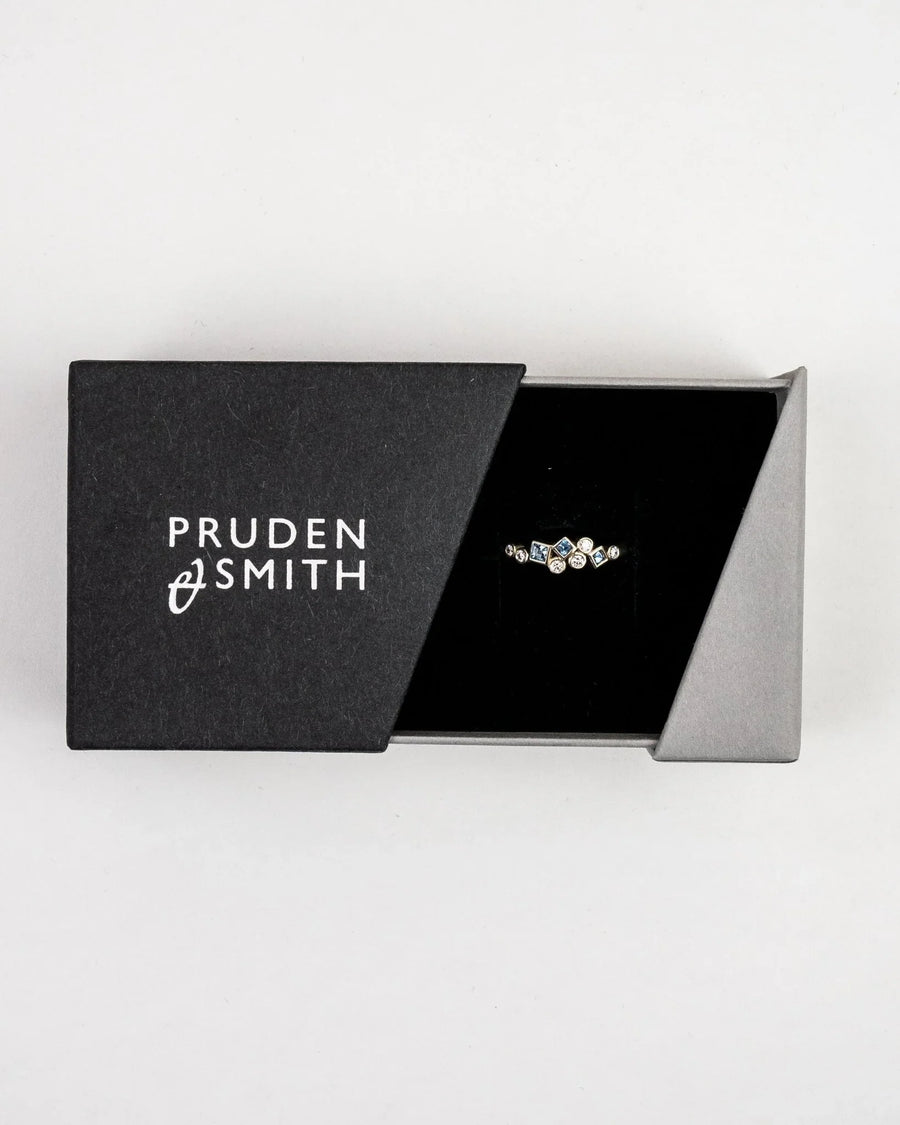 Gold half eternity ring with aquamarine and diamond gemstones in a black box.