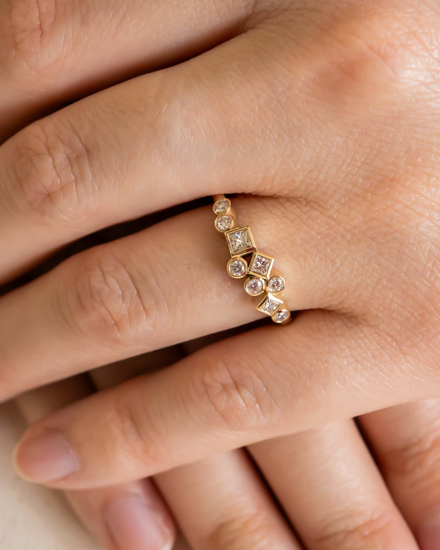 Gold ring with round and square diamonds on a hand.