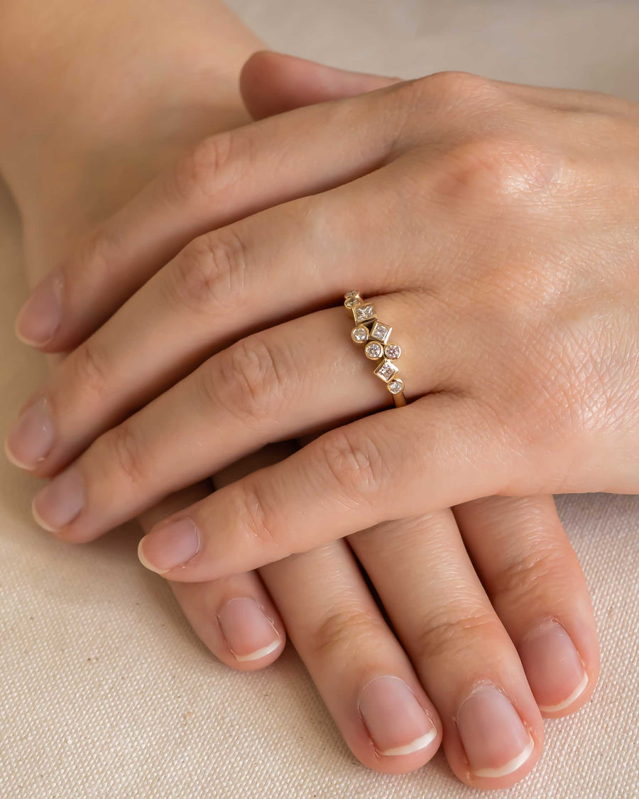 Gold ring with scattered round and square diamonds on a hand.