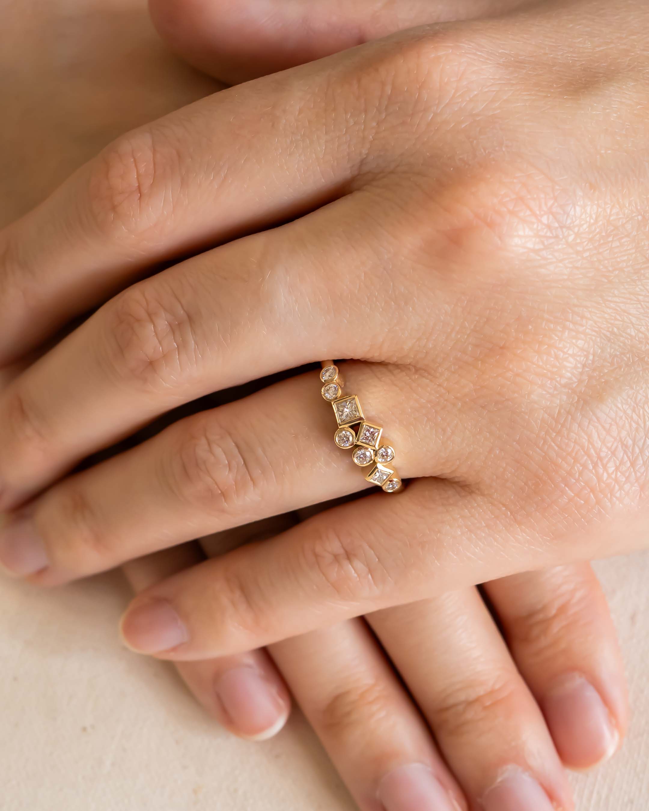 Gold ring with round and square cut diamonds on a hand.
