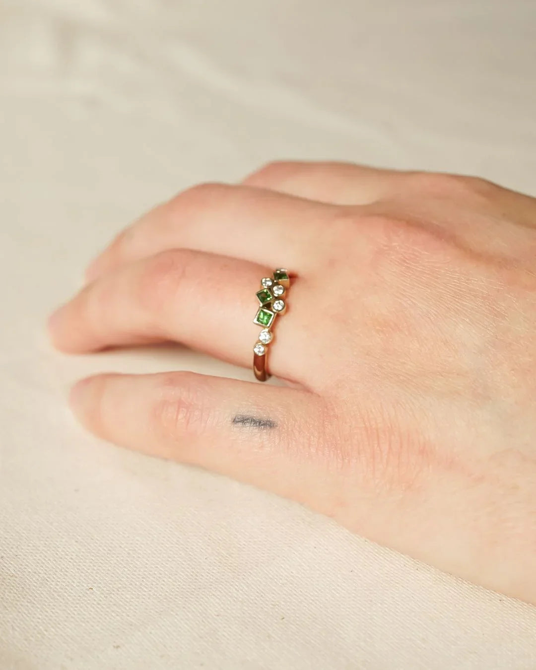 Hand wearing a gold ring with green gemstones and diamonds, showcasing luxury handmade jewellery