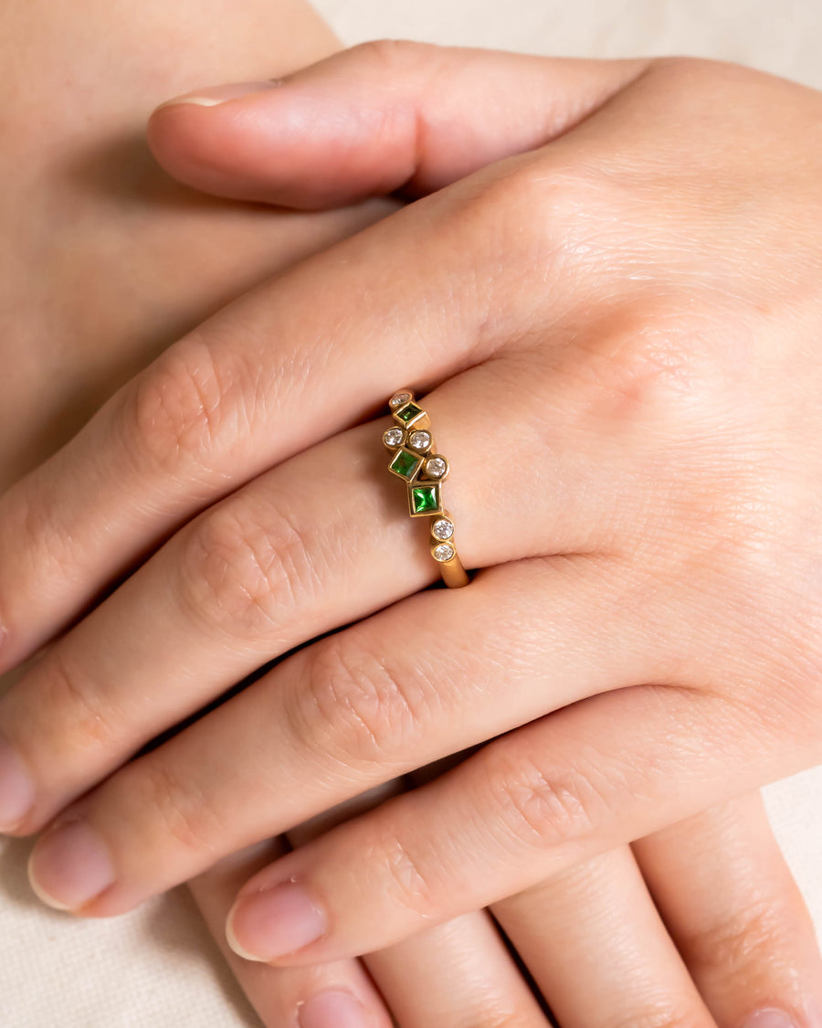 Gold half eternity ring featuring bezel-set round diamonds and square green gemstones on a finger.