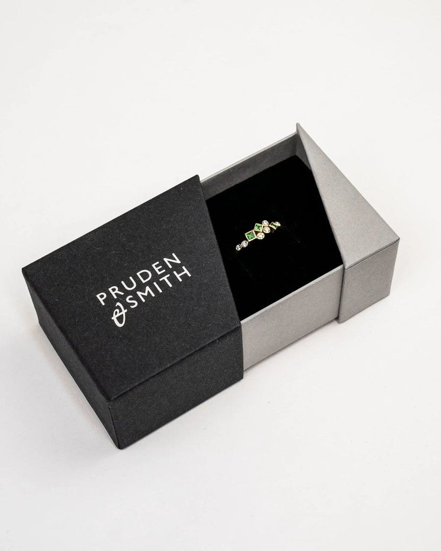 Gold half eternity ring featuring square green gemstones and round diamonds in a black gift box.