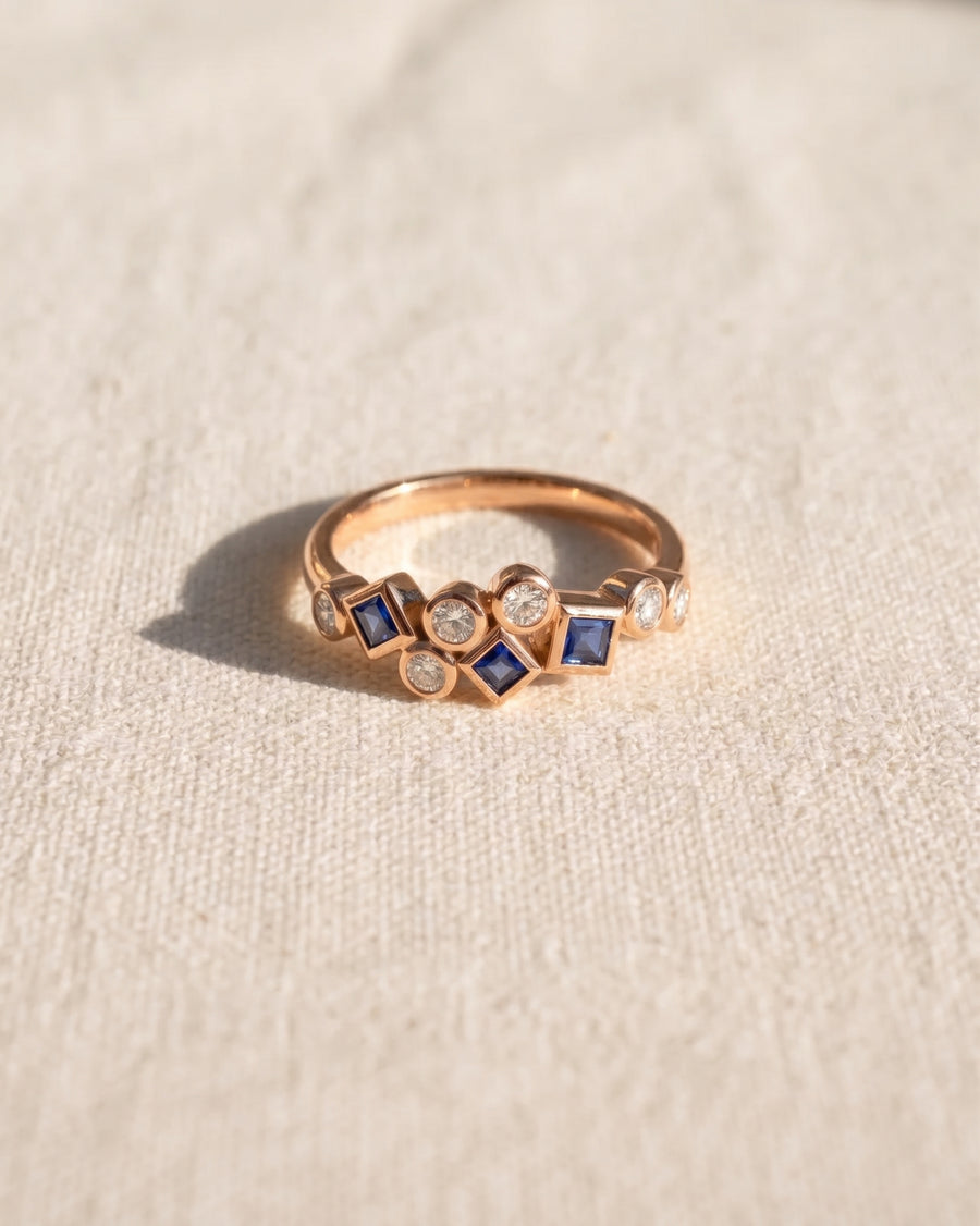 9ct rose gold half eternity ring featuring alternating round diamonds and square-cut blue sapphires.