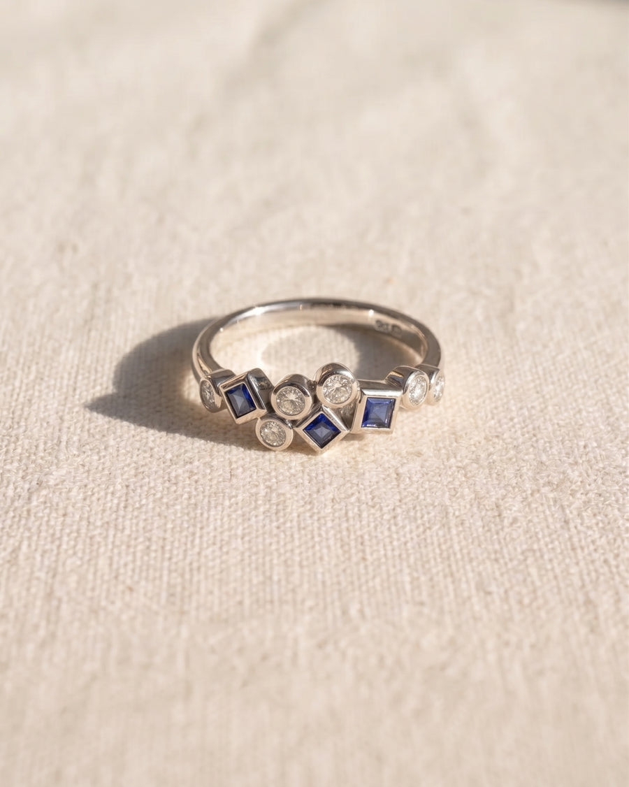 9ct white gold half eternity ring featuring a mix of round diamonds and square-cut blue sapphires.