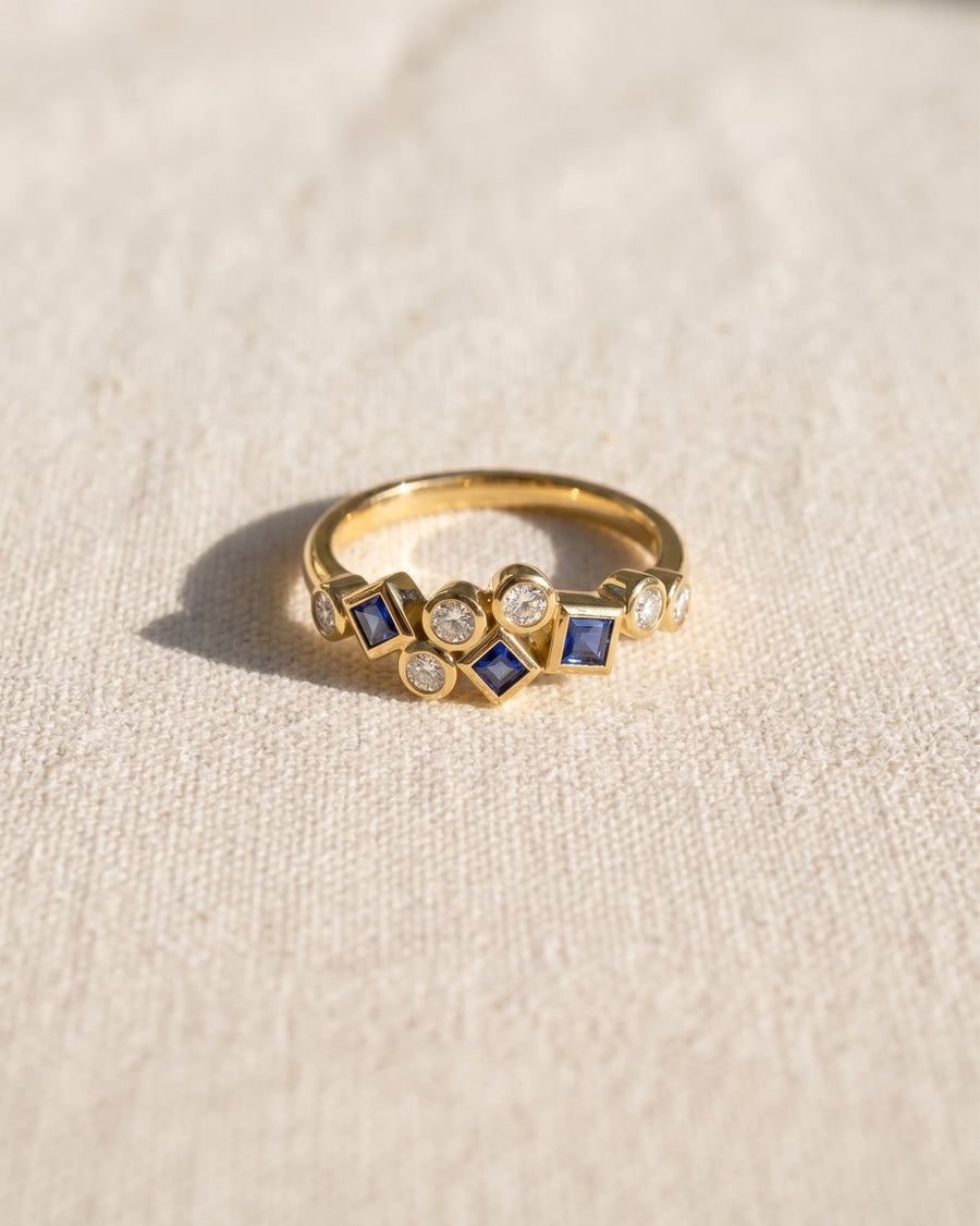 9ct yellow gold half eternity ring featuring a cluster of round diamonds and square blue sapphires.