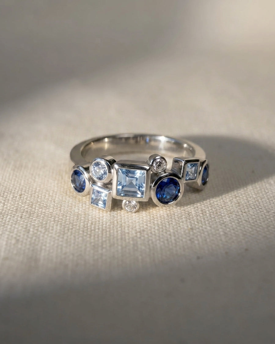 Silver half eternity ring with blue and clear gemstones in various shapes.