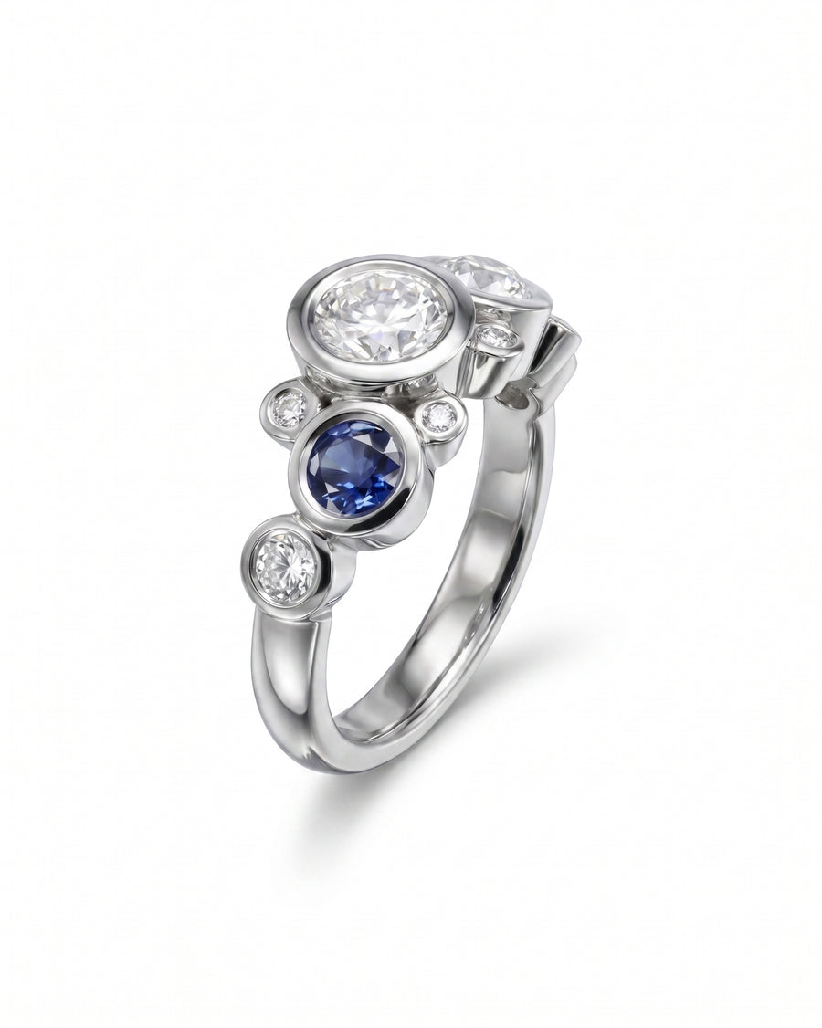 White gold ring with bezel-set round diamonds and a sapphire.