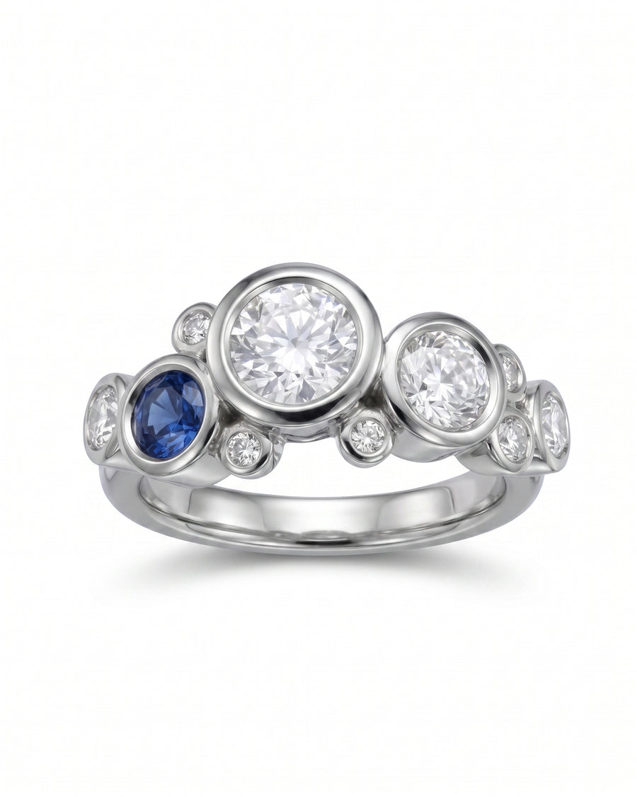 White gold ring with a sapphire and multiple diamonds in a bubble design.