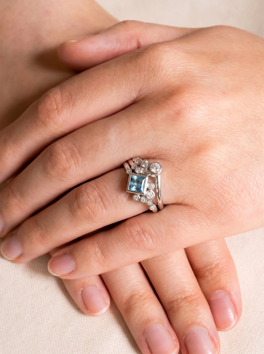 Square aquamarine and diamond ring set in silver metal worn on a finger.