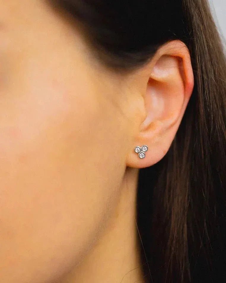 Gold diamond stud earrings with a trefoil design on an ear.