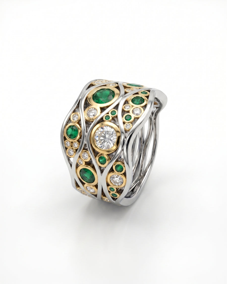 White gold ring with yellow gold accents, round emeralds, and diamonds in a wave design.