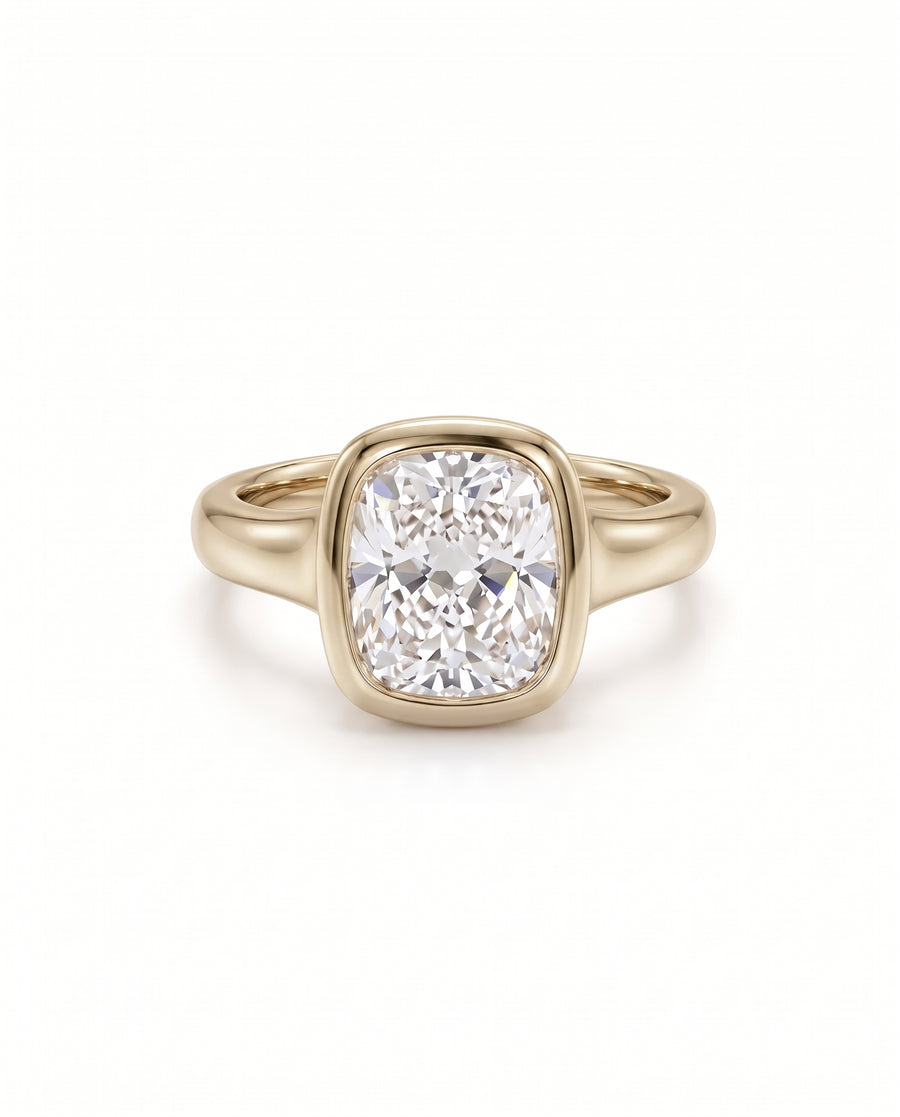 Chunky gold engagement ring featuring a cushion cut diamond set in a smooth bezel setting.