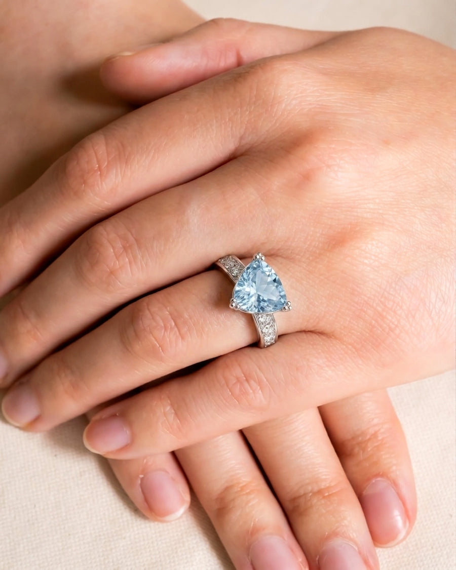 Silver ring with a triangular blue gemstone and pave diamonds on a hand.
