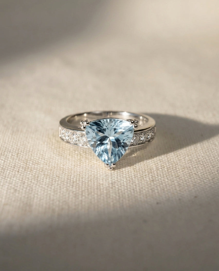 Platinum engagement ring with a light blue trillion-cut gemstone and pavé diamonds.