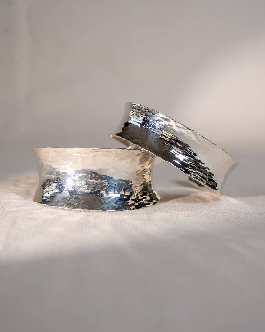 Handcrafted silver hammered cuff bangles with organic, textured finish on neutral fabric
