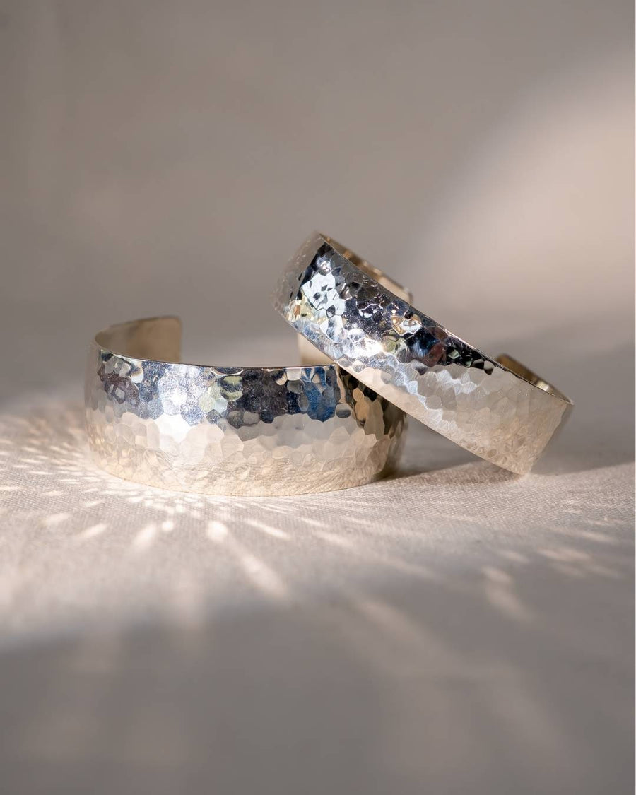 Handmade hammered silver cuff bracelets with textured finish on a neutral fabric background