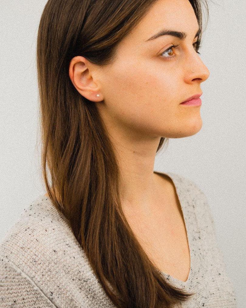 Gold stud earrings with classic round pearls on a woman's ear.