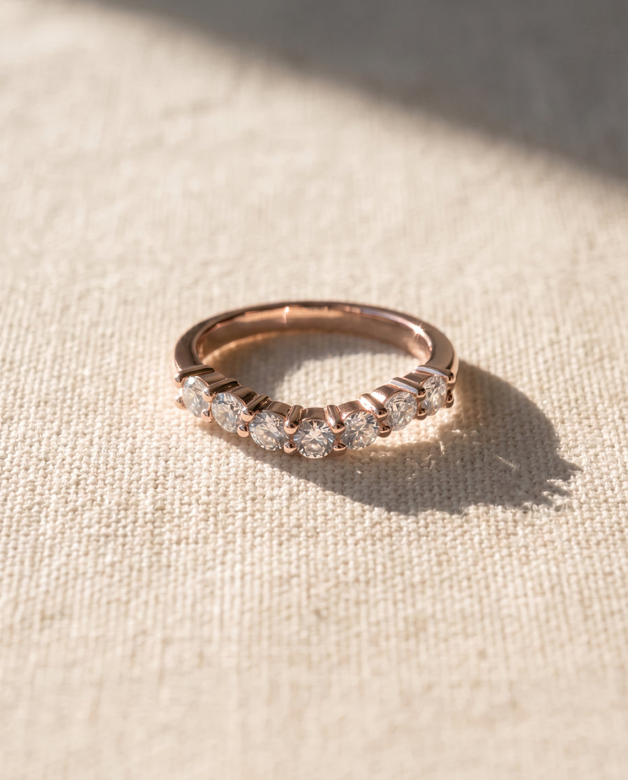 Rose gold wedding ring featuring a row of round cut diamonds in a claw setting on textured fabric.