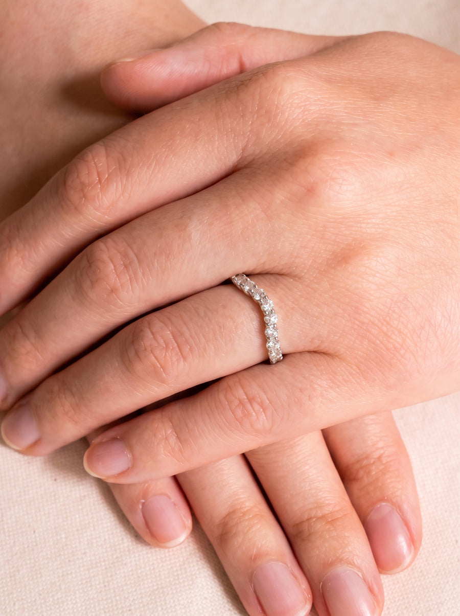 Curved silver wedding band featuring a row of round cut diamonds worn on a finger.