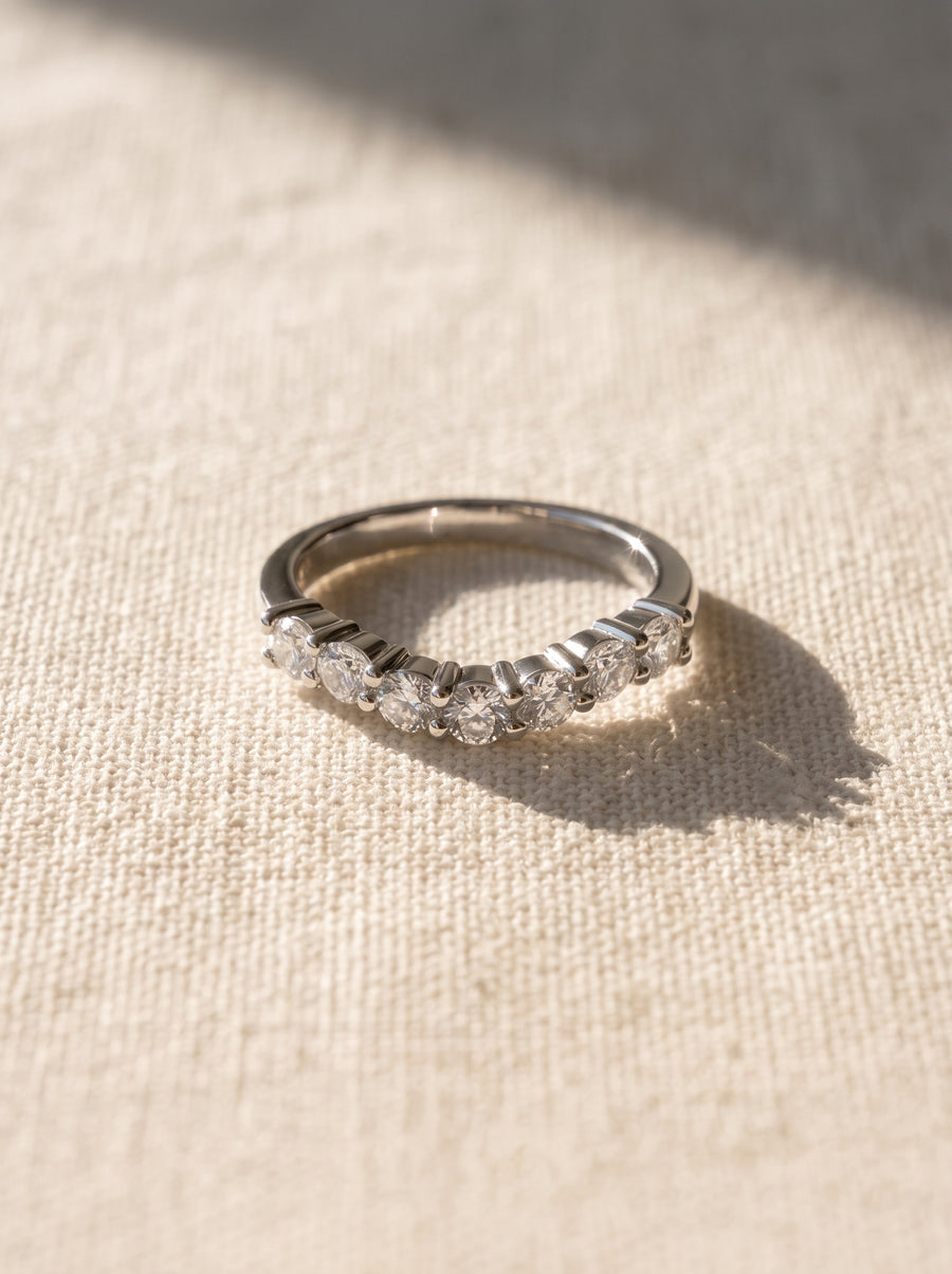 Silver wedding ring with seven round-cut diamonds in a prong setting on a textured fabric background.