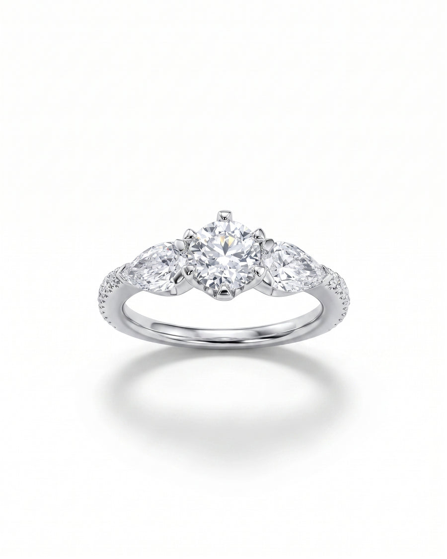 White gold trilogy engagement ring with a round center diamond and two pear-cut side diamonds.