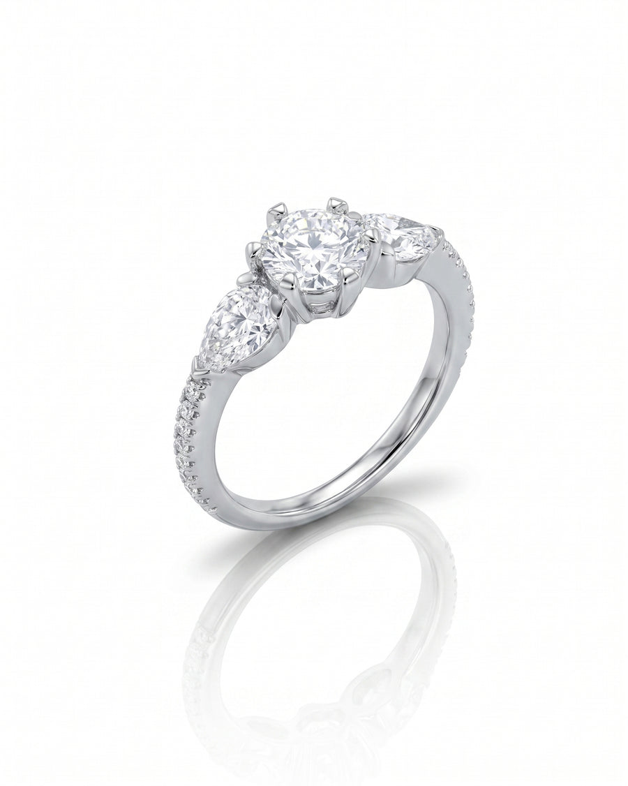Silver engagement ring with a round center diamond and two pear-cut side diamonds.