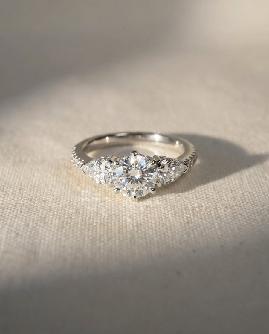 Platinum engagement ring with a round center diamond and two pear-cut side diamonds.