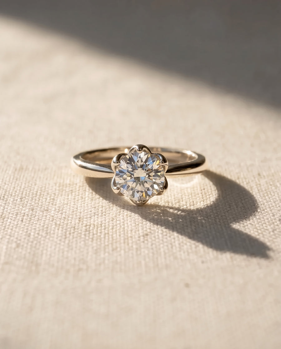 Round brilliant cut diamond engagement ring in a platinum claw setting on a textured fabric surface.