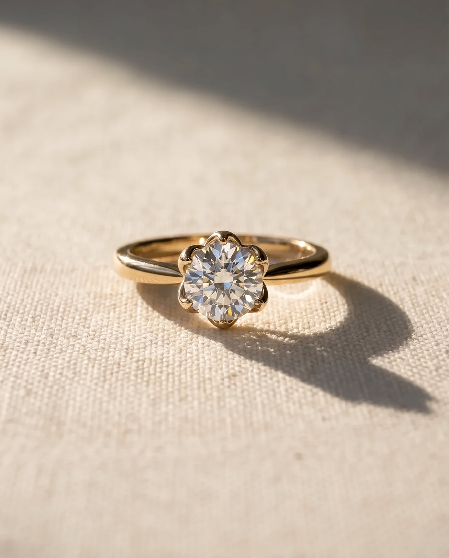 Round brilliant cut diamond engagement ring in a gold claw setting on a textured fabric surface.
