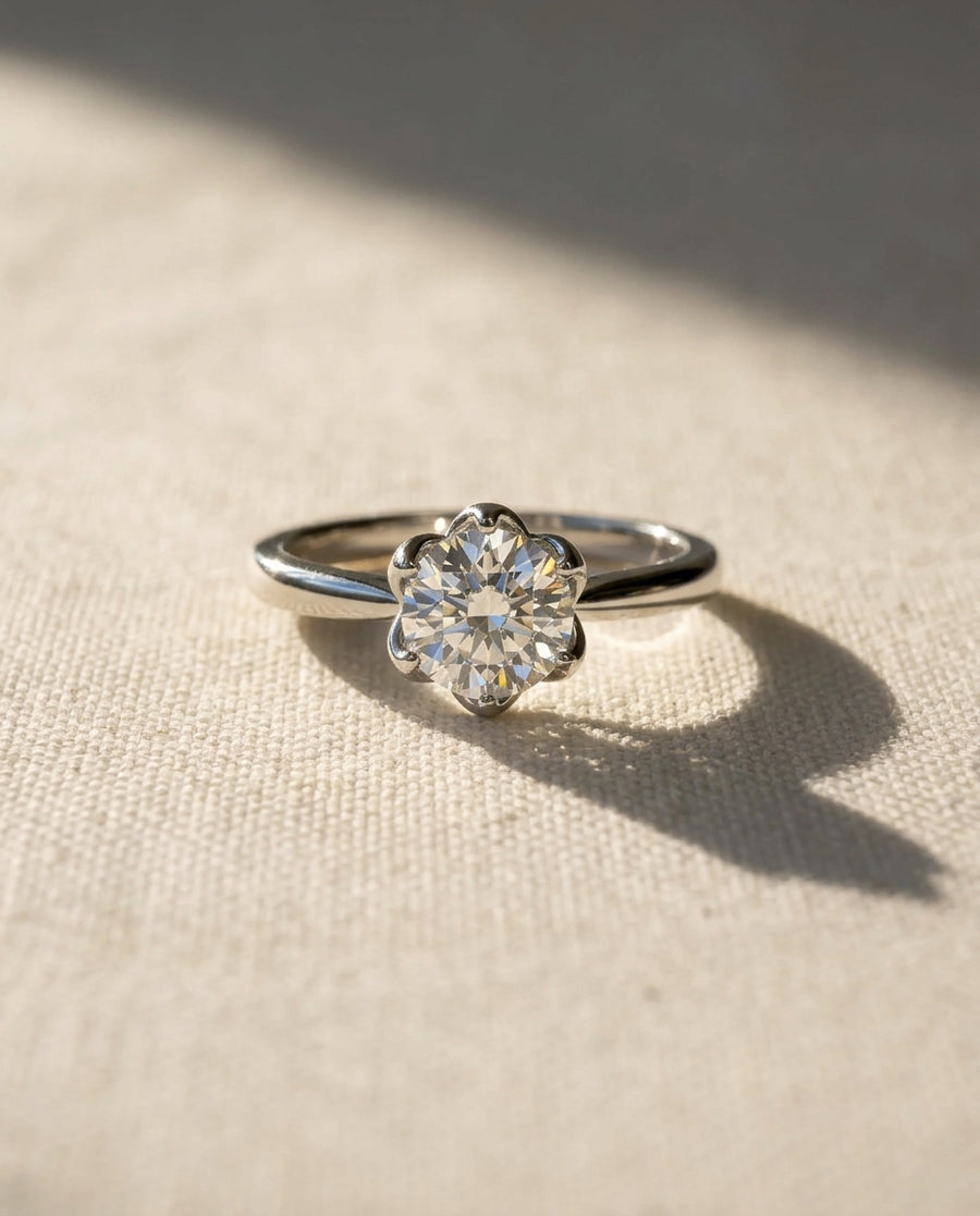 White gold engagement ring with a round diamond in a floral claw setting.