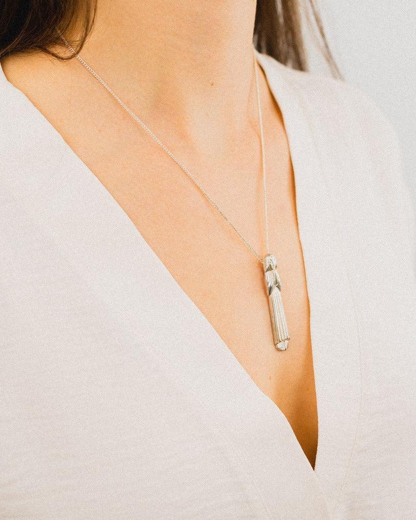 Silver praying girl pendant necklace on woman wearing a white V-neck top