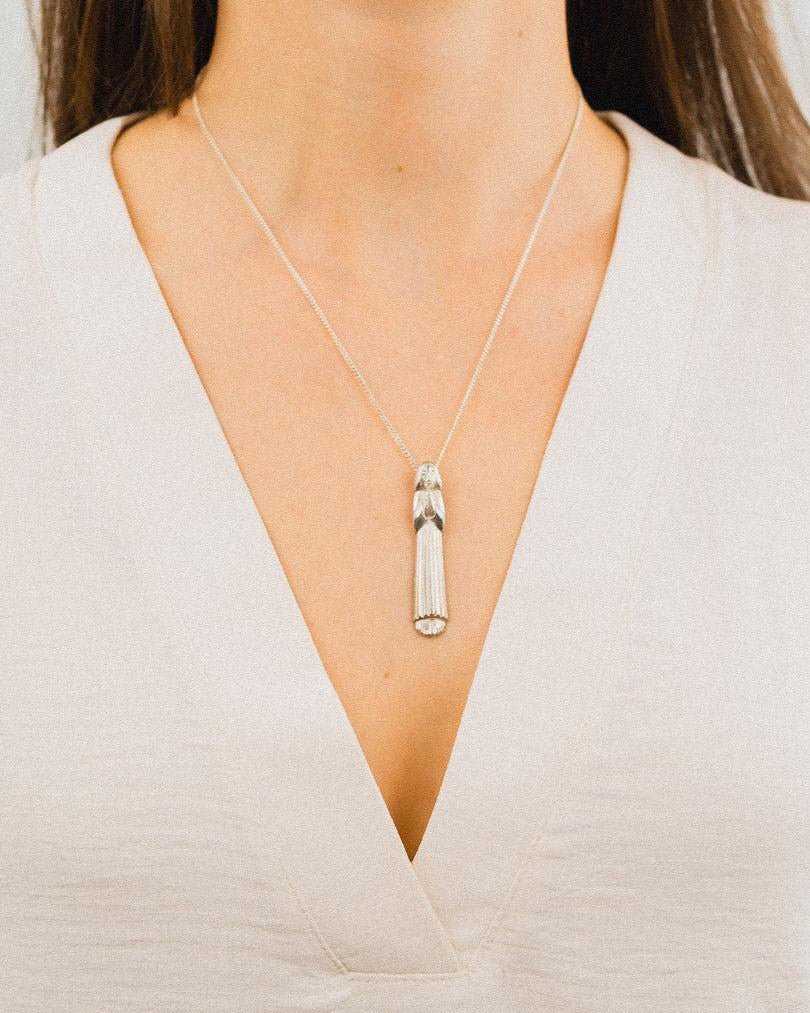 Silver praying girl pendant necklace worn on a delicate chain against a light blouse