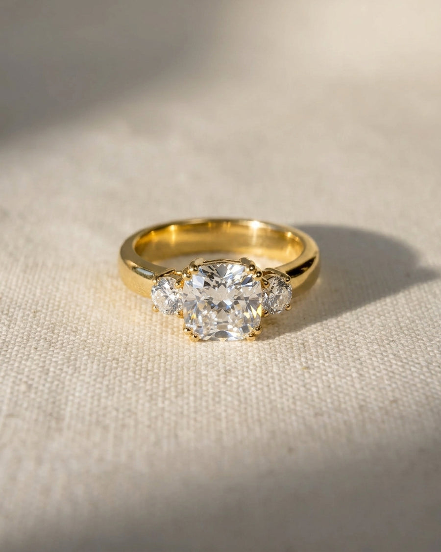 18ct yellow gold trilogy engagement ring with cushion cut and two round lab-grown diamonds.
