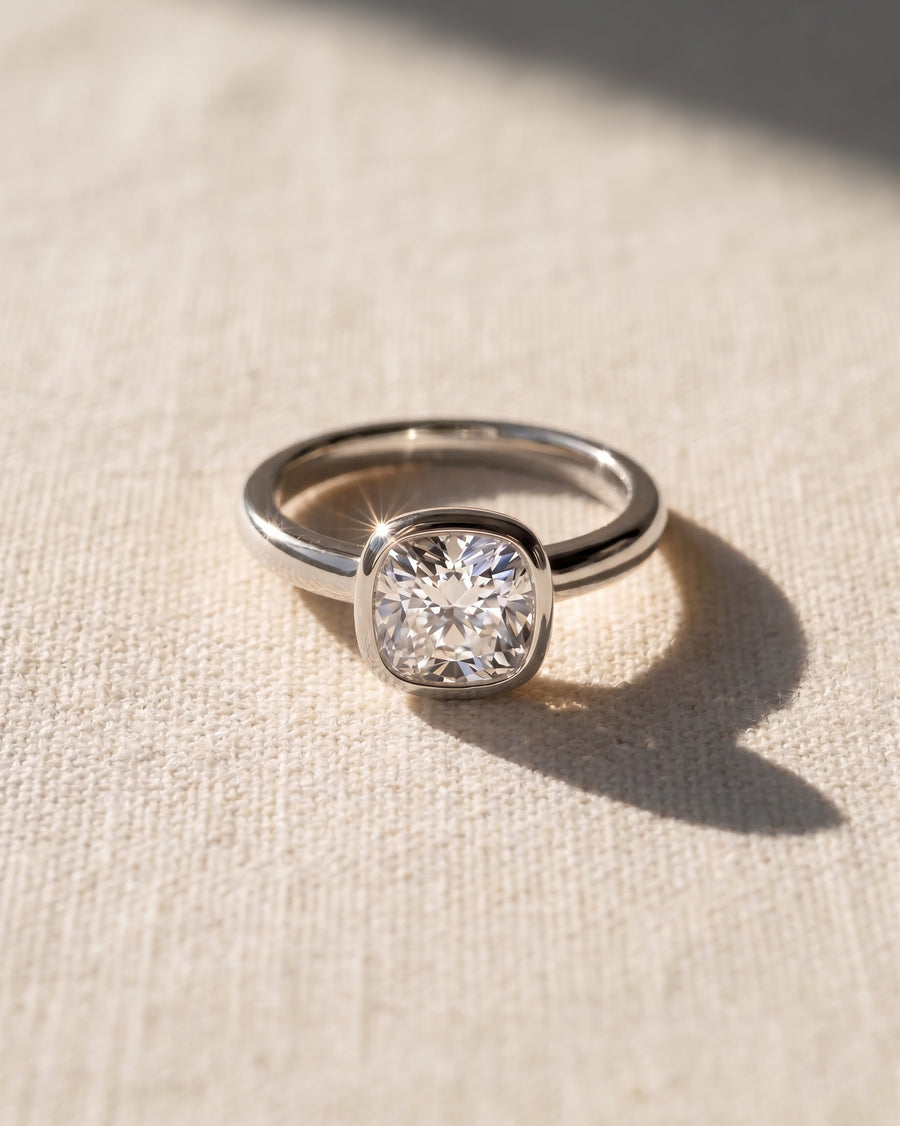 Platinum engagement ring with a 1ct lab grown cushion cut diamond in a bezel setting.
