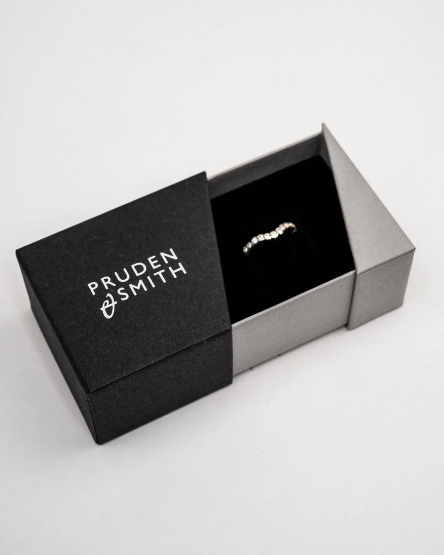Gold diamond-shaped wedding band with small diamonds in a black and gray box.