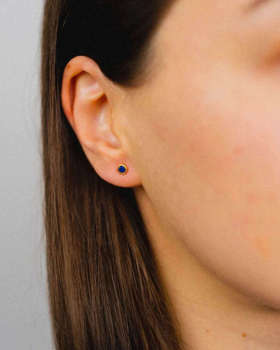 Dainty 18ct gold stud earring with a rough blue gemstone on an ear.